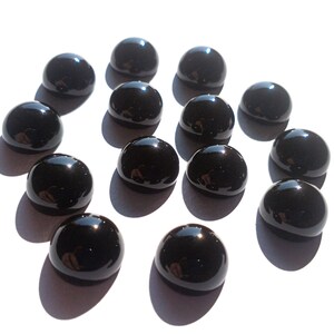 May include: A collection of 13 black round gemstones, likely onyx, displayed on a white surface. The gemstones are smooth and polished, reflecting light.