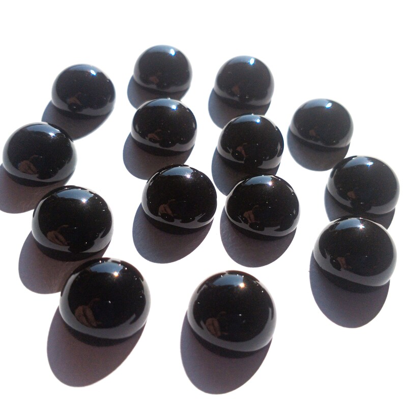 May include: A collection of 13 black round gemstones, likely onyx, displayed on a white surface. The gemstones are smooth and polished, reflecting light.