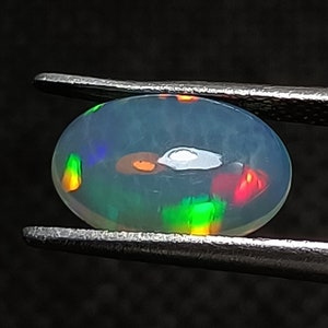 May include: A white oval opal gemstone with a rainbow of colors, including green, red, orange, and blue.