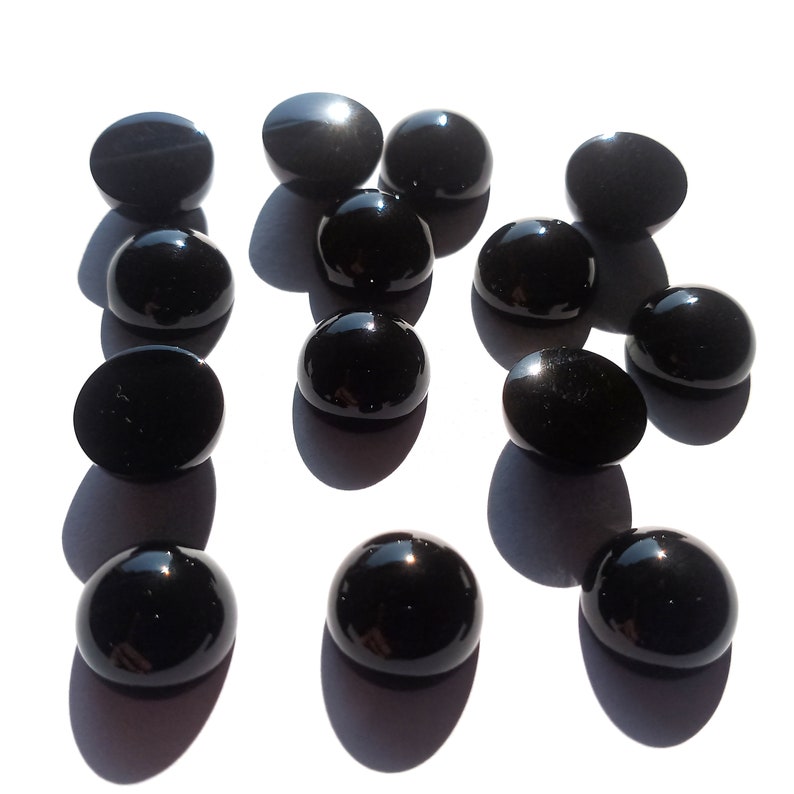 May include: A collection of 13 black gemstone cabochons, each with a smooth, polished surface. The cabochons are arranged in a random pattern on a white background.