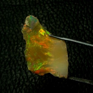 May include: A rough, irregular piece of opal with a translucent, yellow-brown body color. The opal displays flashes of green, orange, and red iridescence.