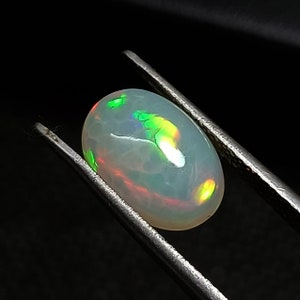 May include: A white oval opal gemstone with green and yellow flashes of color.