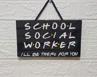 Op de afbeelding: Zwart bord met witte tekst die "S.C.H.O.O.L SOCIAL WORKER I'LL BE THERE FOR YOU" luidt. De letters hebben kleurrijke stippen eromheen.