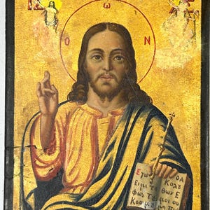 May include: Antique religious icon featuring a central figure with a halo, holding a book and a staff. The icon has a gold background with black borders and includes text in Greek. Angels are depicted in the upper corners.