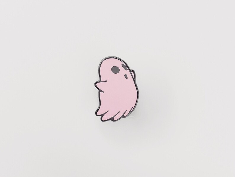 May include: A pink ghost enamel pin with black eyes and a black outline.