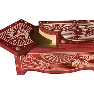 May include: A red wooden box with a hinged lid decorated with gold sun, moon, and star designs. The box has a carved hummingbird and cloud design on the front.