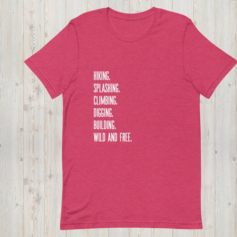 K&ouml;nnte beinhalten: Ein rotes melierter T-Shirt mit wei&szlig;em Text, der "HIKING. SPLASHING. CLIMBING. DIGGING. BUILDING. WILD AND FREE." lautet.