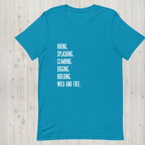 K&ouml;nnte beinhalten: Ein t&uuml;rkisfarbenes T-Shirt mit wei&szlig;em Text, der "HIKING. SPLASHING. CLIMBING. DIGGING. BUILDING. WILD AND FREE." lautet.