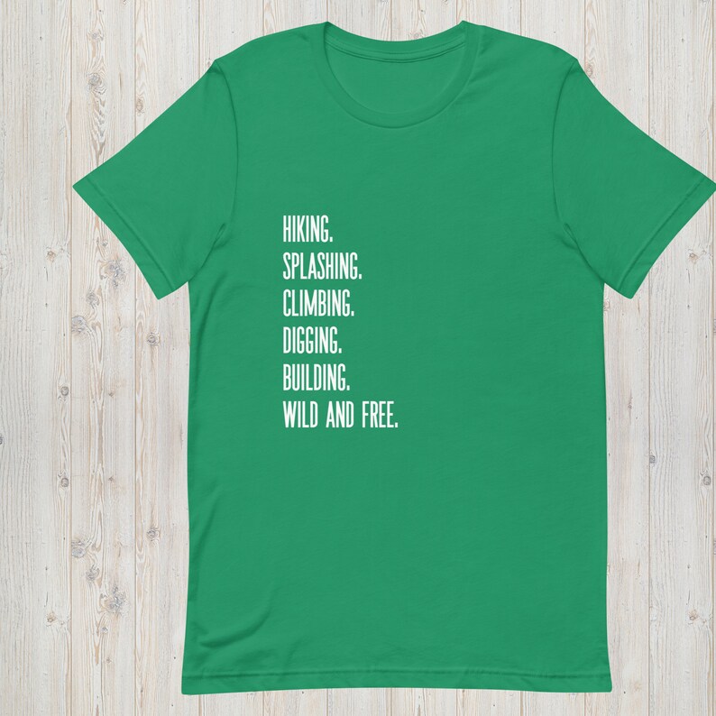 K&ouml;nnte beinhalten: Ein gr&uuml;nes T-Shirt mit wei&szlig;em Text, der "HIKING. SPLASHING. CLIMBING. DIGGING. BUILDING. WILD AND FREE." lautet.