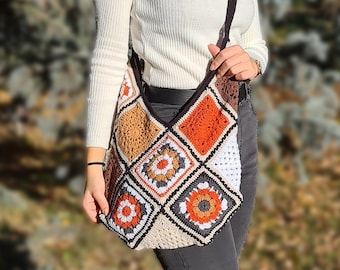 May include: A woman wearing a white turtleneck sweater and black jeans is carrying a crocheted shoulder bag with a colorful geometric pattern. The bag has a brown strap and is worn over the shoulder.