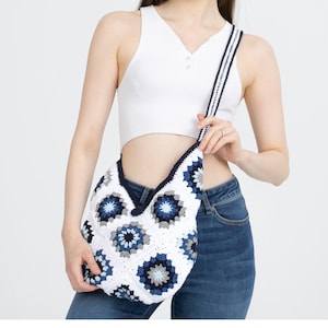 May include: A white crochet bag with a blue and white geometric pattern. The bag has a long strap and is worn over the shoulder.