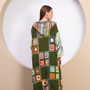 Puede incluir: Una larga chaqueta de punto de ganchillo verde con un diseño de patchwork colorido. La chaqueta tiene capucha y mangas largas.