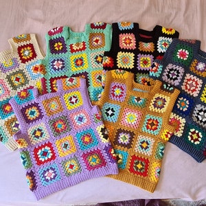 May include: A collection of colourful crocheted vests with a granny square pattern. The vests are in various colours, including purple, blue, green, yellow, orange, and red.