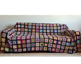 May include: A black crocheted throw blanket with colourful squares, draped over a sofa.