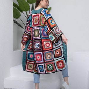 May include: A long, teal crochet cardigan with a patchwork design of colorful squares. The cardigan has a loose fit and long sleeves.