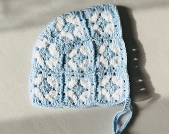 May include: A light blue crocheted baby bonnet with a white pattern and a long tie.