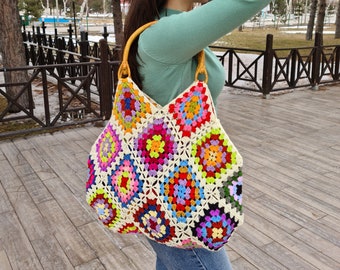 May include: A large, colorful crochet tote bag with a wooden handle. The bag is made of granny squares in various shades of red, orange, yellow, green, blue, purple, and pink.