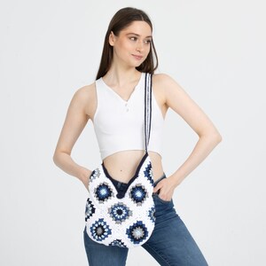 May include: A white crocheted shoulder bag with a blue and white geometric pattern. The bag has a long strap and is worn over the shoulder.