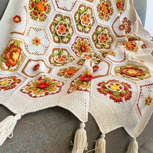 May include: A crocheted throw blanket with a white background and colorful floral patterns. The blanket has tassels on the edges.