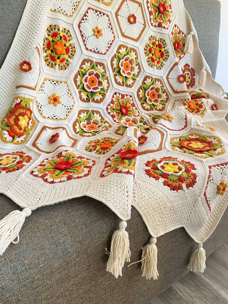 May include: A crocheted throw blanket with a white background and colorful floral patterns. The blanket has tassels on the edges.