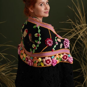 May include: A black crochet shawl with a floral design. The shawl features pink, yellow, and green flowers, as well as two embroidered birds.