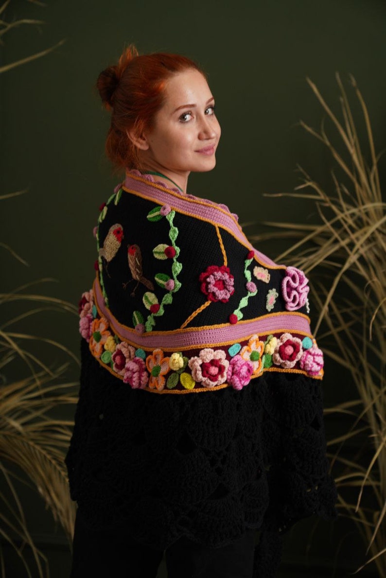 May include: A black crochet shawl with a floral design. The shawl features pink, yellow, and green flowers, as well as two embroidered birds.