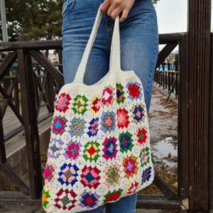 May include: A white crochet tote bag with colorful granny squares. The bag has a long strap and is made of cotton yarn.