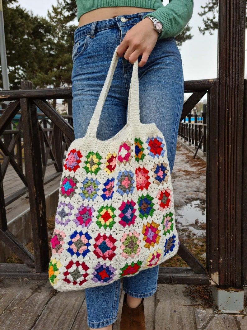 May include: A white crochet tote bag with colorful granny squares. The bag has a long strap and is made of cotton yarn.