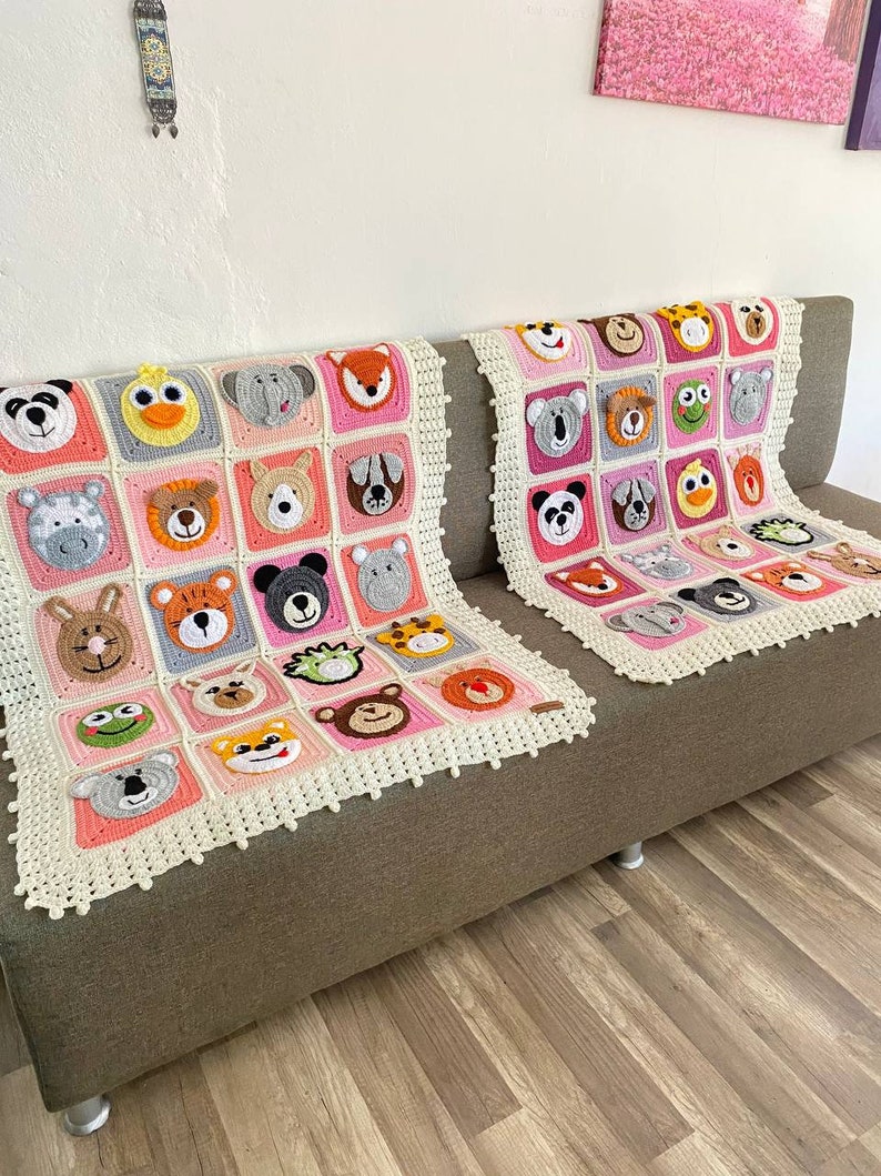 Puede incluir: Dos mantas de crochet en un esquema de color rosa y blanco. Cada manta presenta una cara de animal diferente en cada cuadrado. Las mantas est&aacute;n en un sof&aacute; marr&oacute;n.