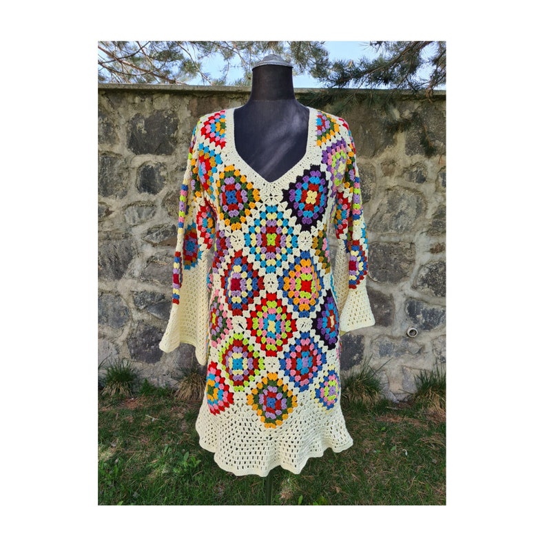 May include: A white crochet dress with a colorful geometric pattern. The dress has a V-neck and long sleeves.