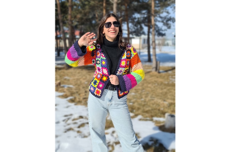 Puede incluir: Una chaqueta de crochet colorida con un dise&ntilde;o de patchwork. La chaqueta tiene mangas largas y un cierre de bot&oacute;n. La persona que lleva la chaqueta est&aacute; sonriendo y mirando a la c&aacute;mara.