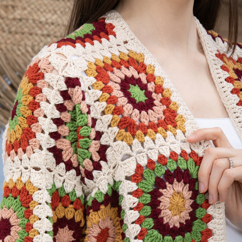 Pu&ograve; includere: Un cardigan lavorato a uncinetto con un motivo geometrico in tonalit&agrave; crema, rosso, arancione, verde e marrone.
