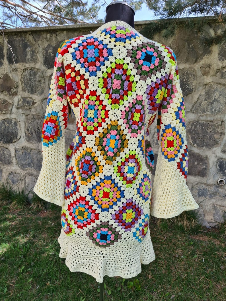 May include: A colorful crochet cardigan with a granny square pattern. The cardigan has long sleeves with bell bottoms and a ruffled hem.