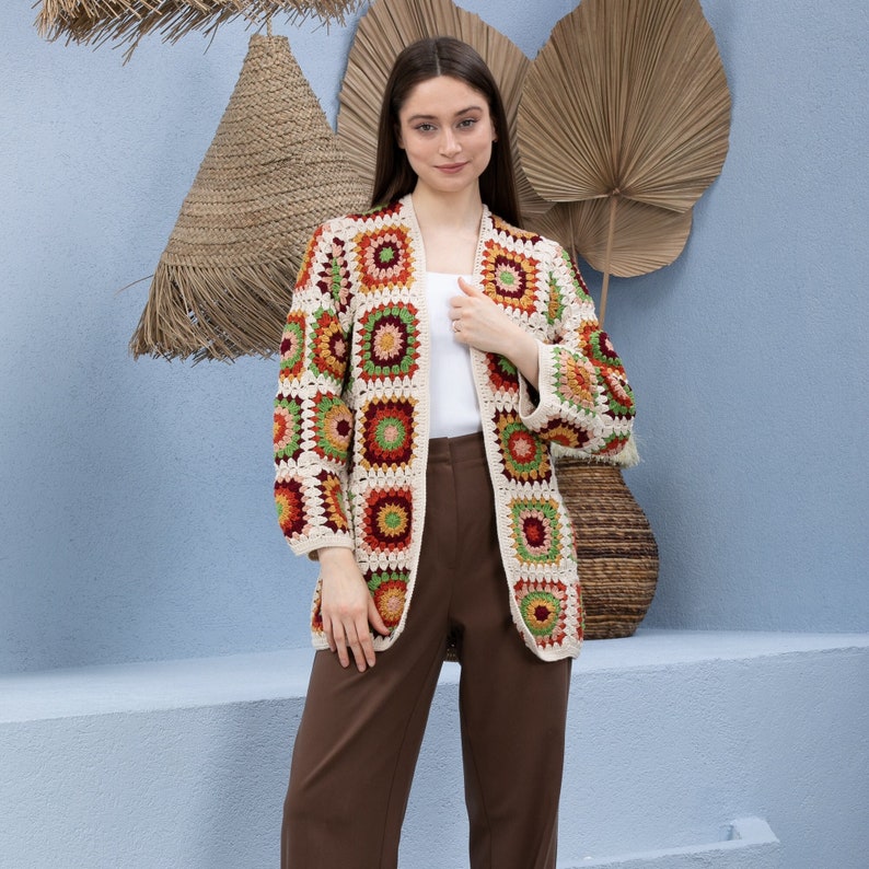 Pu&ograve; includere: Un cardigan in crochet a maniche lunghe con un motivo geometrico in tonalit&agrave; di rosso, arancione, verde e beige. Il cardigan ha una vestibilit&agrave; rilassata e una scollatura aperta.