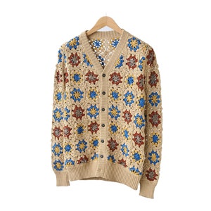 Puede incluir: Un cárdigan de crochet beige con un patrón cuadrado en tonos de azul, rojo y amarillo.