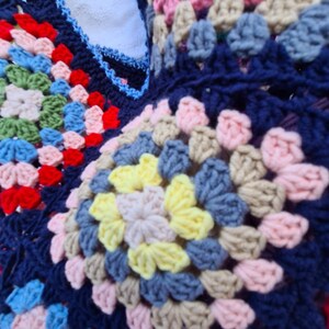 May include: Close-up of a colorful crocheted blanket with a variety of colors including blue, pink, yellow, and green. The blanket is made of a soft, textured yarn and has a granny square pattern.