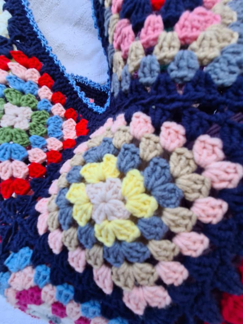 May include: Close-up of a colorful crocheted blanket with a variety of colors including blue, pink, yellow, and green. The blanket is made of a soft, textured yarn and has a granny square pattern.