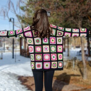 May include: A black crochet cardigan with colorful square patterns. The cardigan has long sleeves and a loose fit.
