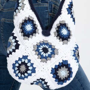 May include: A white crochet tote bag with blue and gray granny squares. The bag has a wide, open top and a single strap.