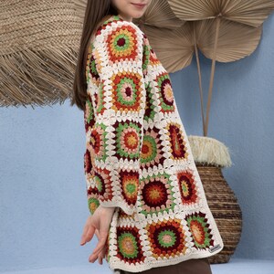 Pu&ograve; includere: Un cardigan bianco all'uncinetto con un motivo geometrico colorato. Il cardigan ha una vestibilit&agrave; ampia e maniche lunghe. Il motivo presenta quadrati con accenti rossi, arancioni, verdi e marroni.