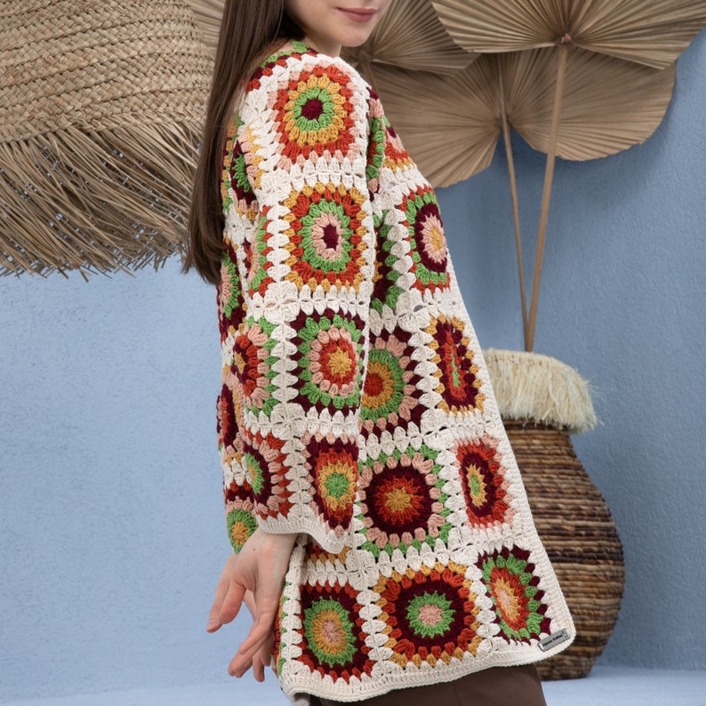 Pu&ograve; includere: Un cardigan bianco all'uncinetto con un motivo geometrico colorato. Il cardigan ha una vestibilit&agrave; ampia e maniche lunghe. Il motivo presenta quadrati con accenti rossi, arancioni, verdi e marroni.