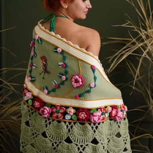 May include: A green crocheted shawl with a floral design and a small bird embroidered on it. The shawl has a scalloped edge and a fringe.
