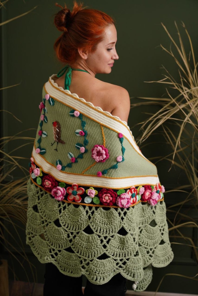May include: A green crocheted shawl with a floral design and a small bird embroidered on it. The shawl has a scalloped edge and a fringe.