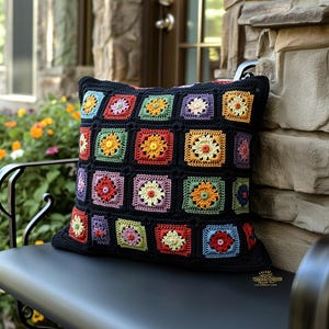 Könnte beinhalten: Ein schwarzes Häkelkissen mit einem bunten Blumenmuster. Das Kissen besteht aus Quadraten mit verschiedenen farbigen Blumen in jedem Quadrat. Das Kissen liegt auf einer schwarzen Bank.