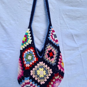 May include: A colorful crocheted tote bag with a blue strap. The bag is made of granny squares in various colors, including pink, red, yellow, green, and blue.
