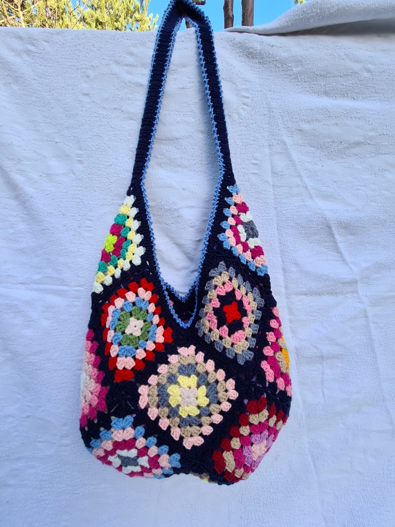 May include: A colorful crocheted tote bag with a blue strap. The bag is made of granny squares in various colors, including pink, red, yellow, green, and blue.