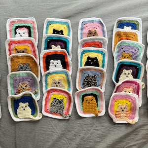 May include: A collection of 18 colorful crocheted squares featuring different cat designs. Each square has a white border and a rainbow-colored background with a cat in the center. The cats are all different colors and have different expressions.
