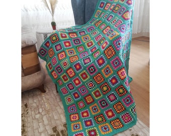 May include: A teal crochet throw blanket with a colourful granny square pattern. The blanket is draped over a chair in a living room.