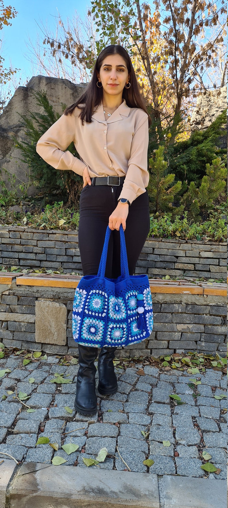 May include: A blue crocheted tote bag with white and light blue squares. The bag has a tassel and white pom-poms.