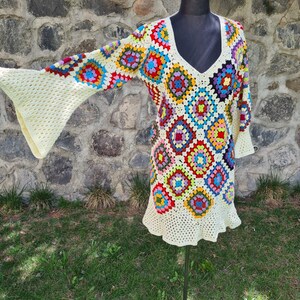May include: A crocheted dress with a granny square pattern in various colors, including red, blue, green, yellow, and white. The dress has a V-neck and long sleeves with bell bottoms.